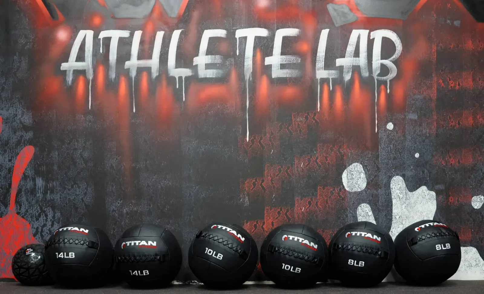 A row of medicine balls, 8 to 14 pounds, beneath the Athlete Lab mural