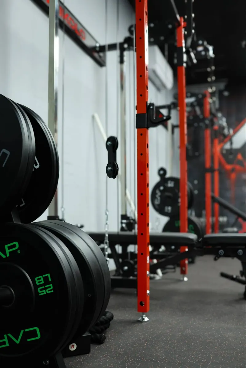 Bumper plates stacked beside red squat racks and adjustable benches on the training floor
