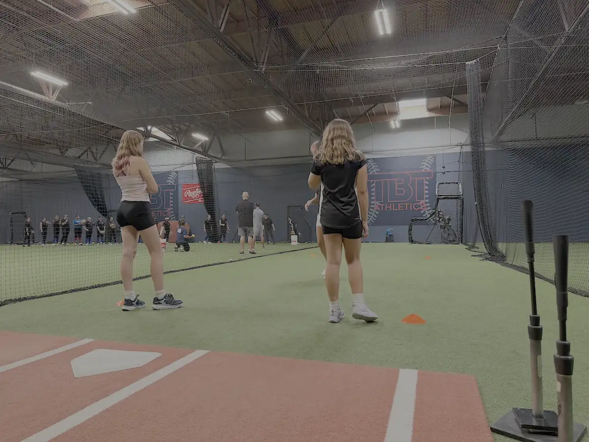 Athletes working a drill on indoor turf, with cones laid out and batting nets overhead